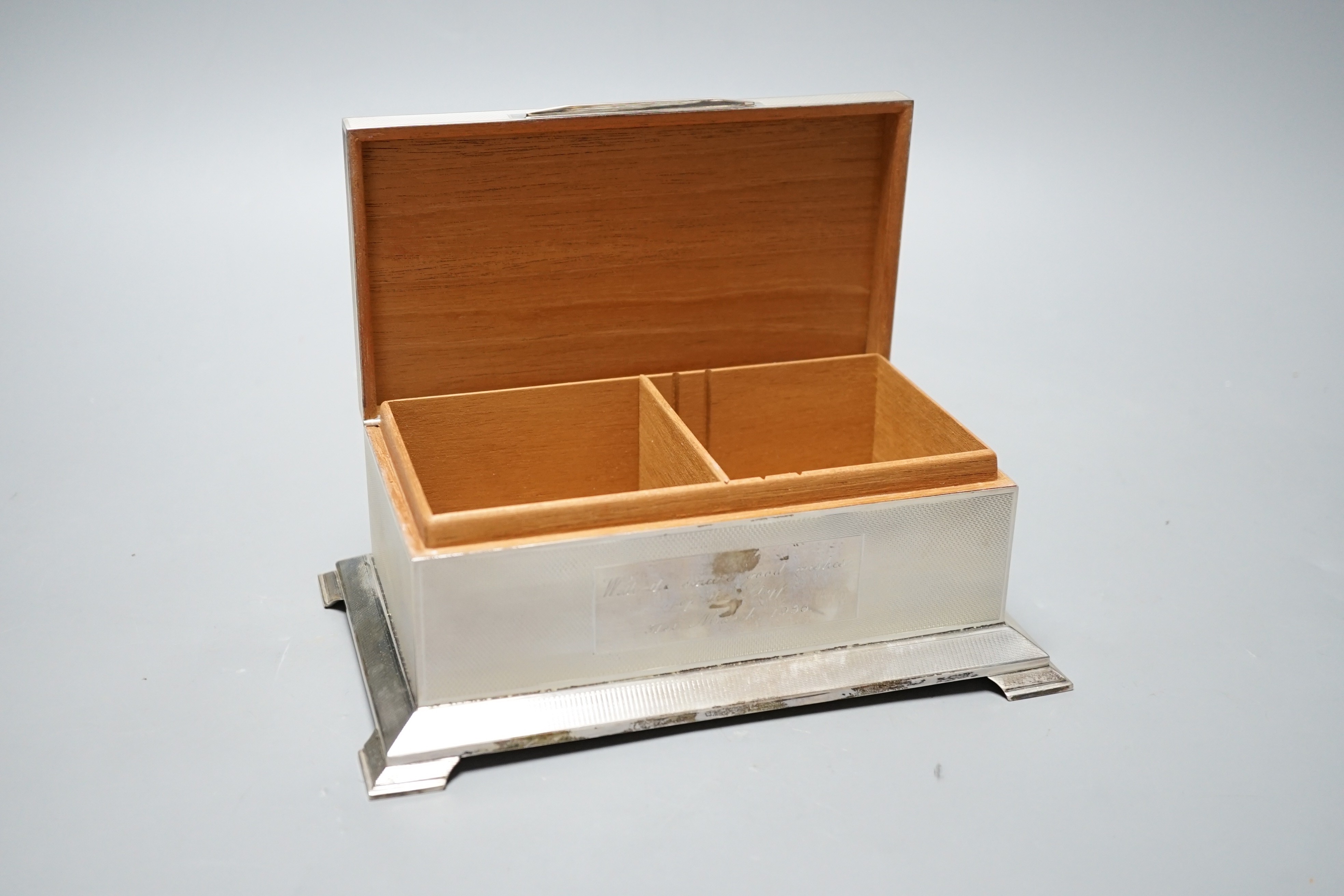 A George VI engine turned silver mounted rectangular cigarette box, Alexander Clark Co Ltd, Birmingham, 1948, with engraved inscription, on bracket feet, 20.4cm.